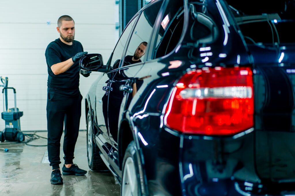 Focused Male car wash worker in black gloves polishes the mirror of car using polishing sponge
